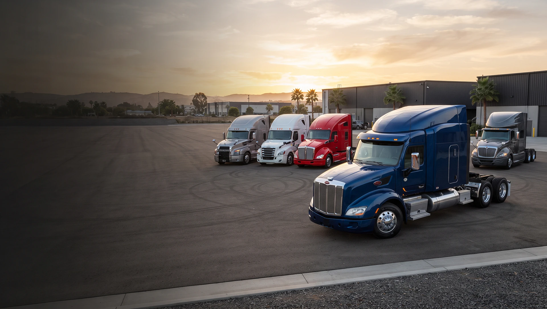 Semi trucks parked in a lot at sunset
